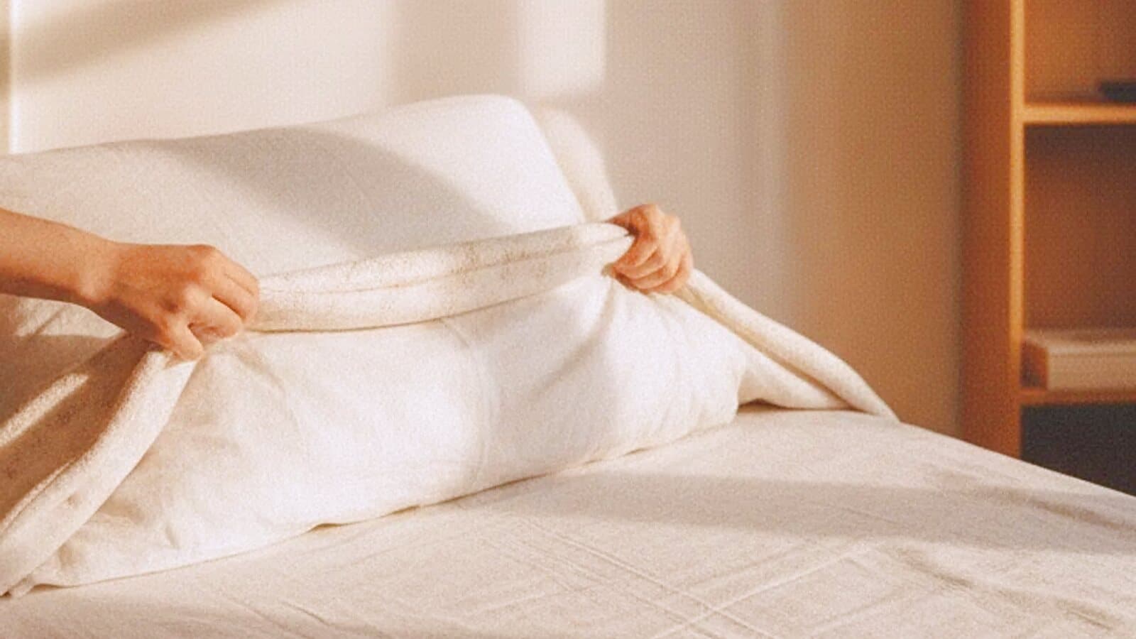 Zwei Hände ziehen in einem hellen Zimmer eine frische Decke über ein Bett